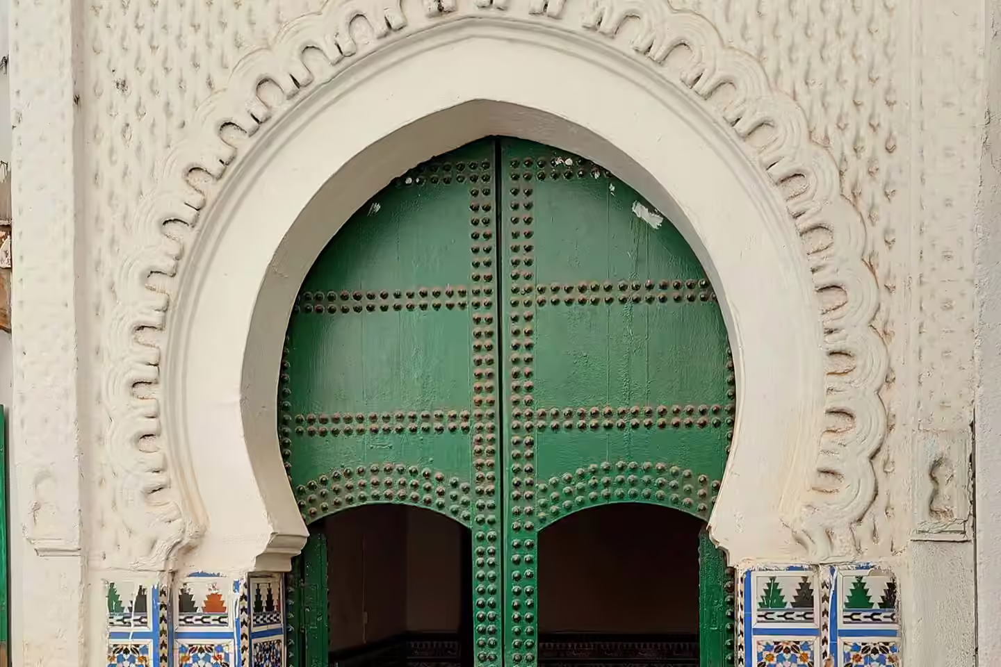 Une porte de mosquée verte encadrée de plâtre sculpté et de zellige à Chefchaouen
