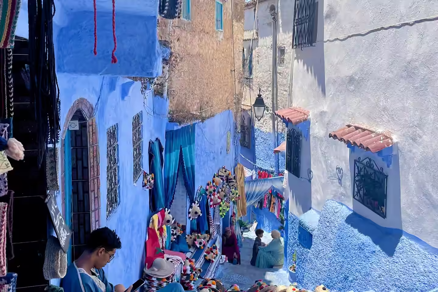Des babouches à pompons et des tissages à vendre dans une ruelle de Chefchaouen