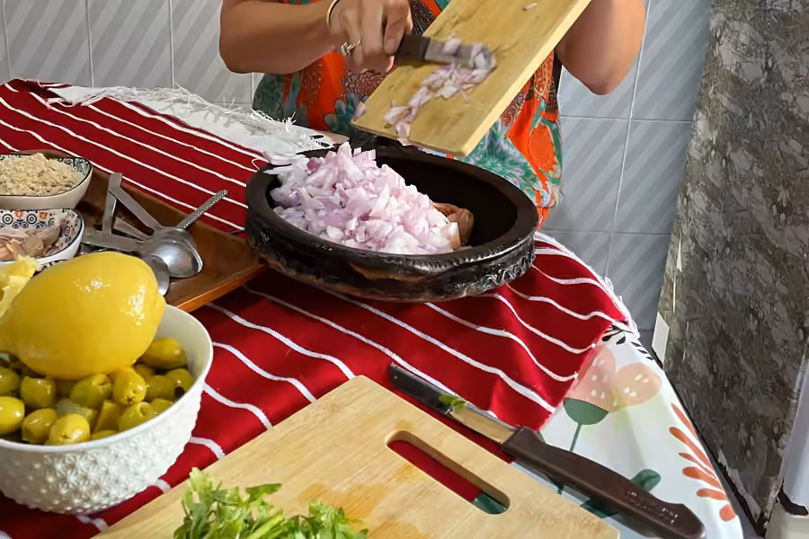 A guest chopping onions for a tagine at a home kitchen table