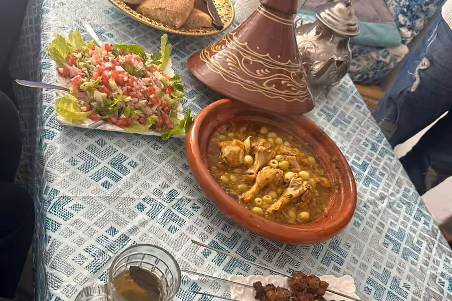 Un tajine de poulet, des salades et du thé à la menthe sur une table en carreaux après un cours de cuisine