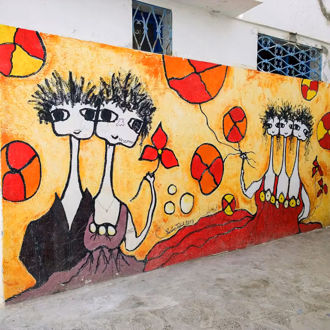 Un mural de figuras de cuello largo y flores rojas en una pared blanca de la medina de Asilah