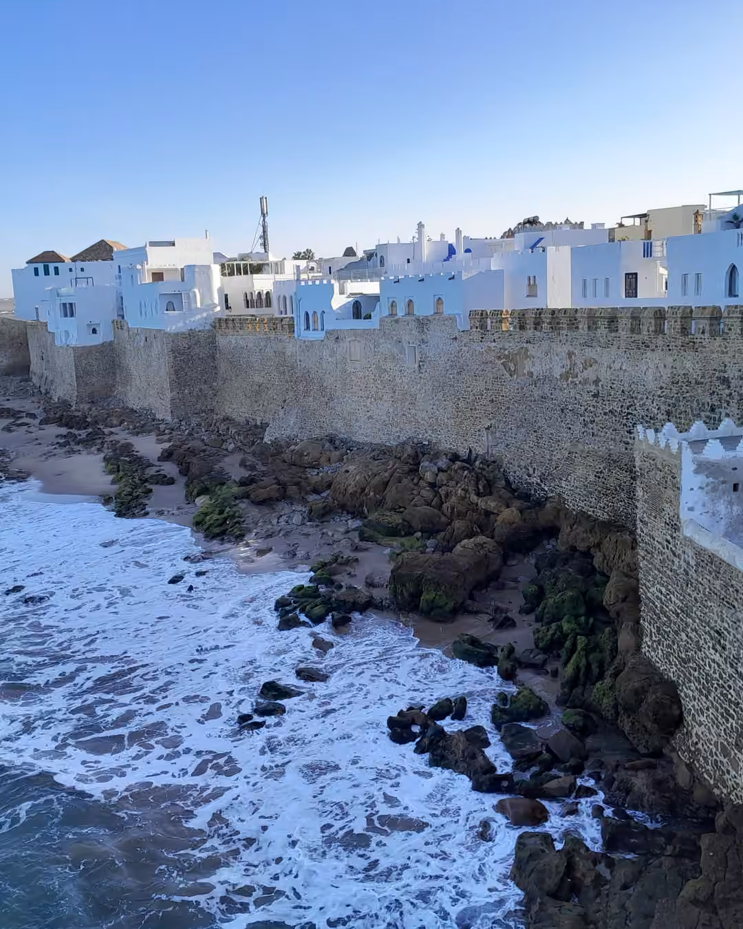 Las murallas de Asilah sobre las olas del Atlántico, con las casas blancas de la medina en lo alto