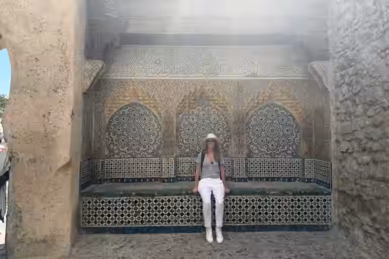 Una fuente de azulejos en un nicho de la Kasbah de Tánger, con una viajera sentada en su banco